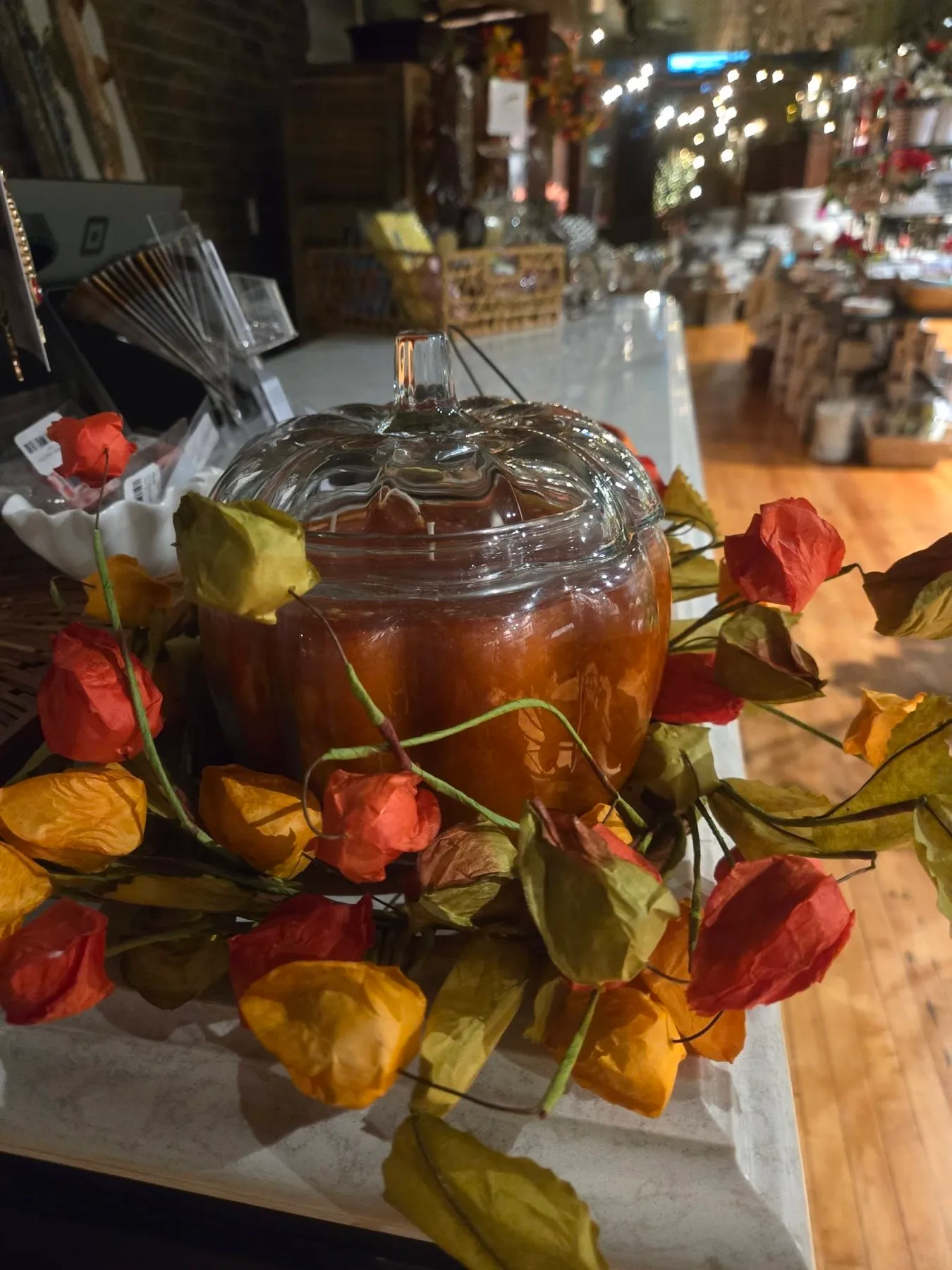 A glass pumpkin jar filled with an amber candle, ringed with paper lanterns