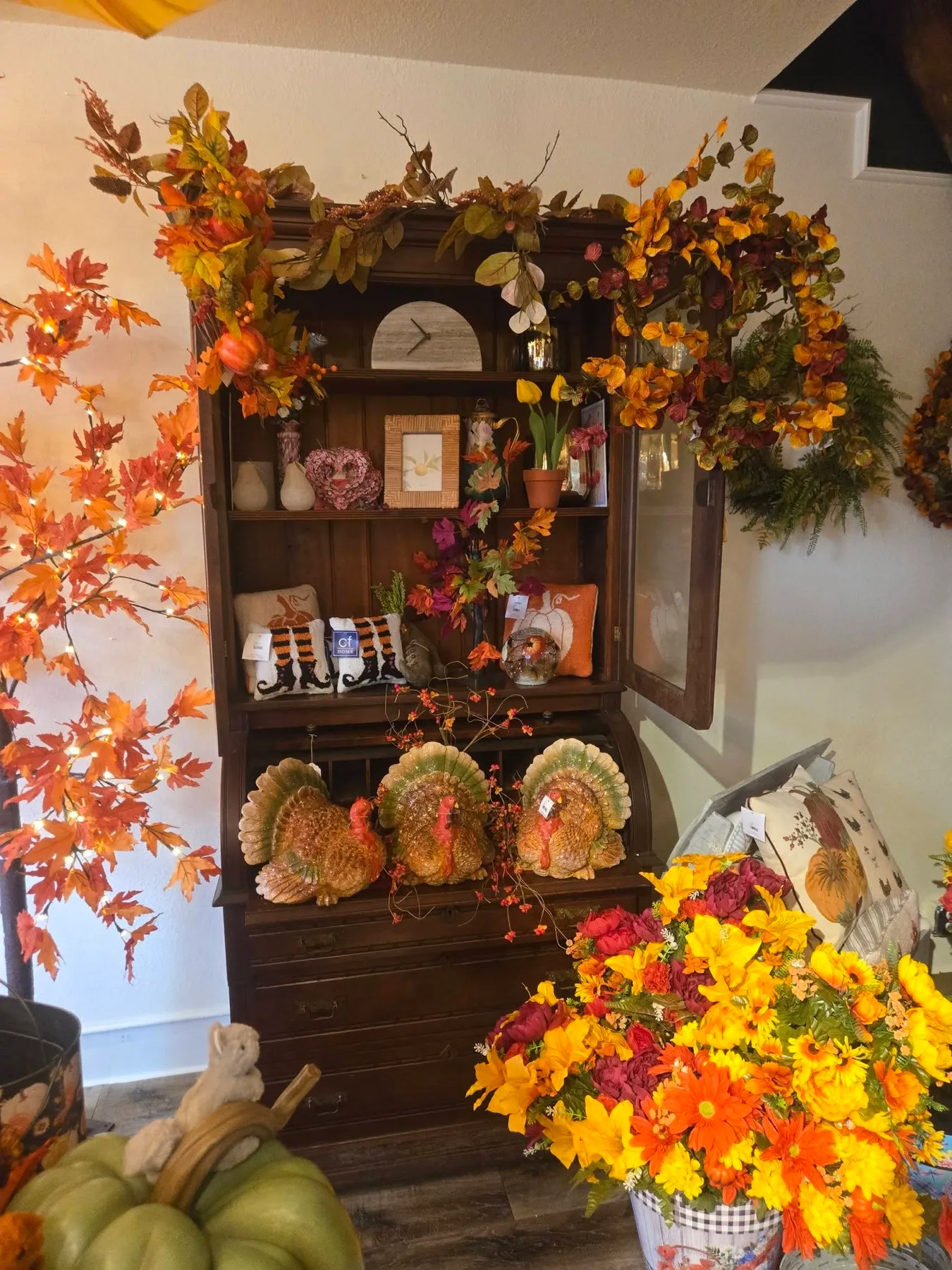 An antique hutch wrapped in orange maple leaves, with ceramic turkeys and fall florals