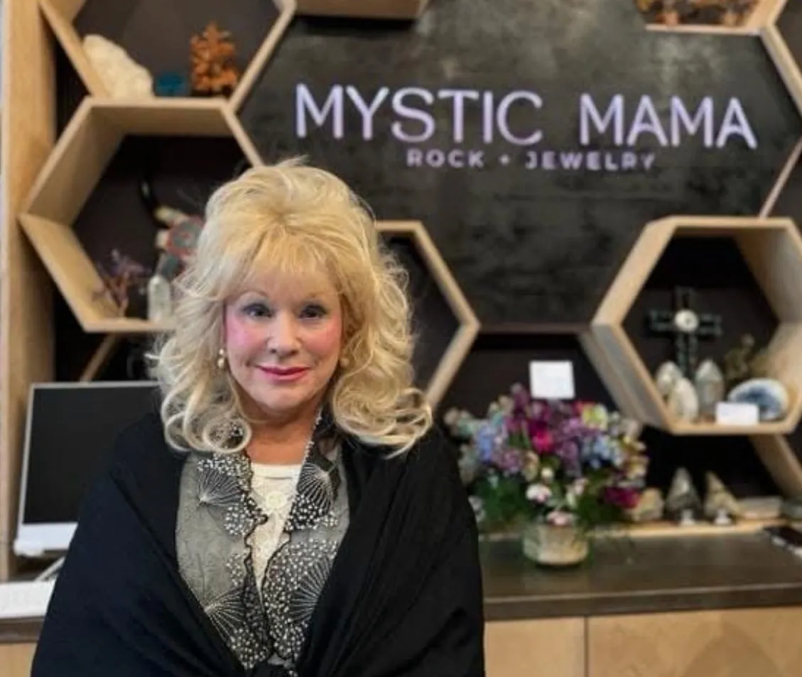 Shary Duff in front of the Mystic Mama sign and its honeycomb shelves of crystals