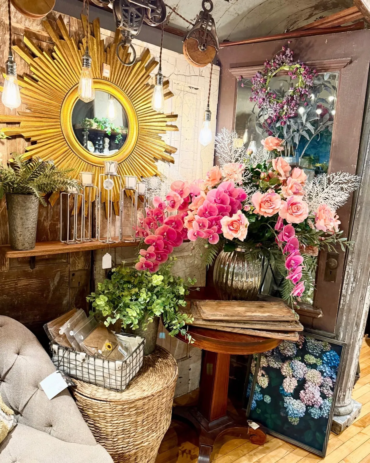 A gold sunburst mirror above pink orchids, a brass vase and stacked books