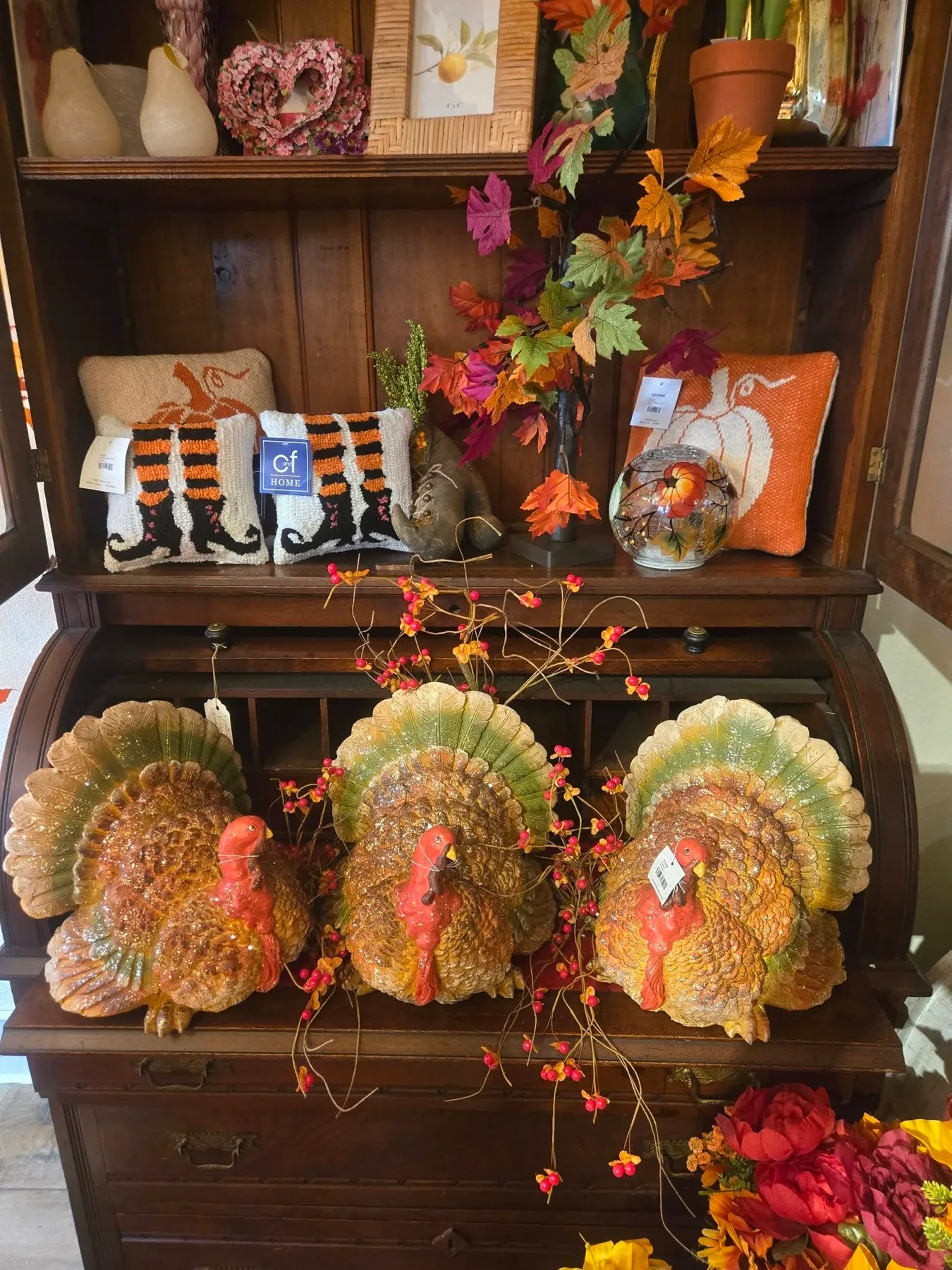 Three ceramic turkeys on a roll-top desk under fall leaves and pillows